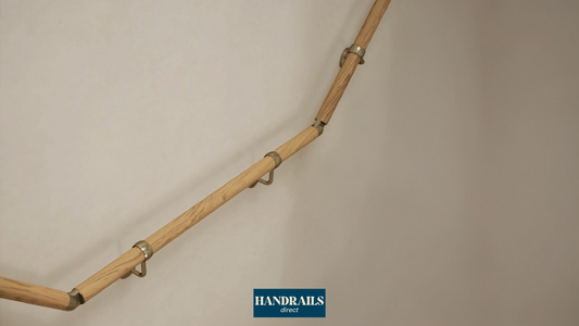 Handrails Direct wooden oak handrail pole attached to a cream wall with an antique brass adjustable elbow and support bracket