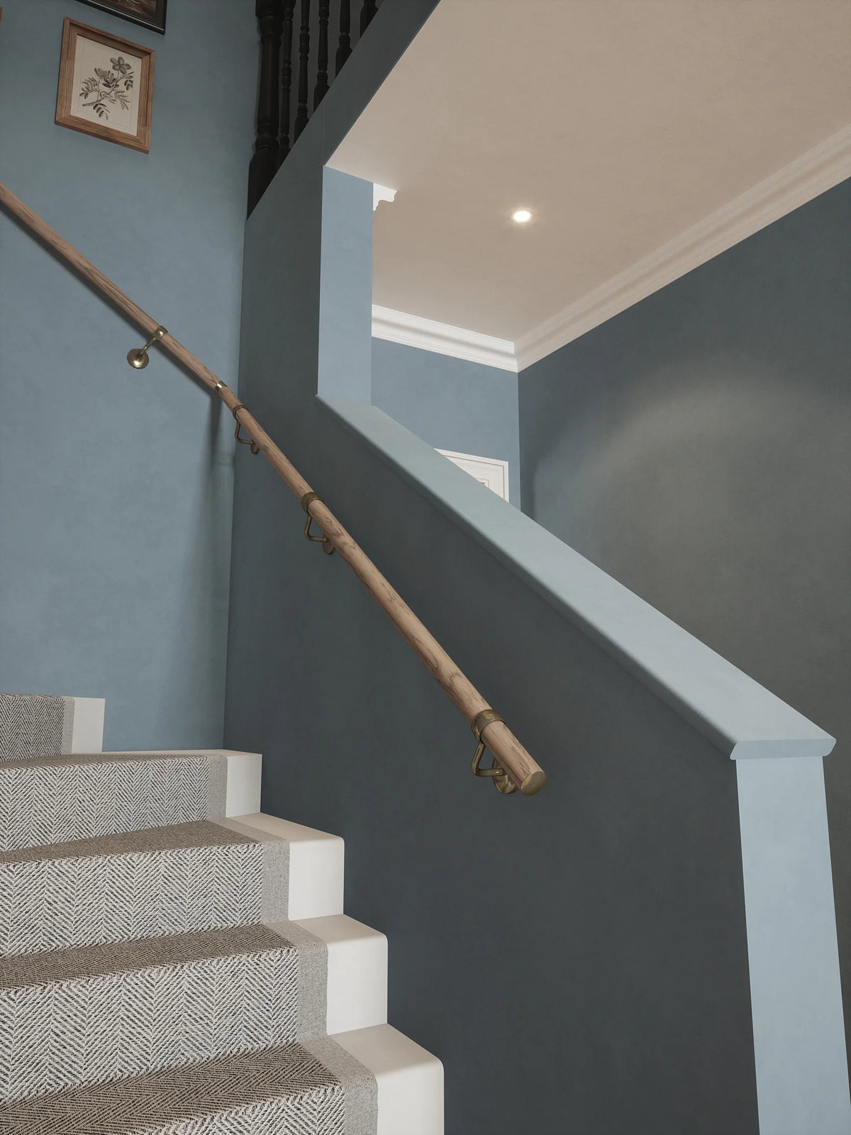 Angled view of Oversley Walnut Single Winder Handrail with Loxley Antique Brass brackets beside carpeted stairs against a blue-grey wall.