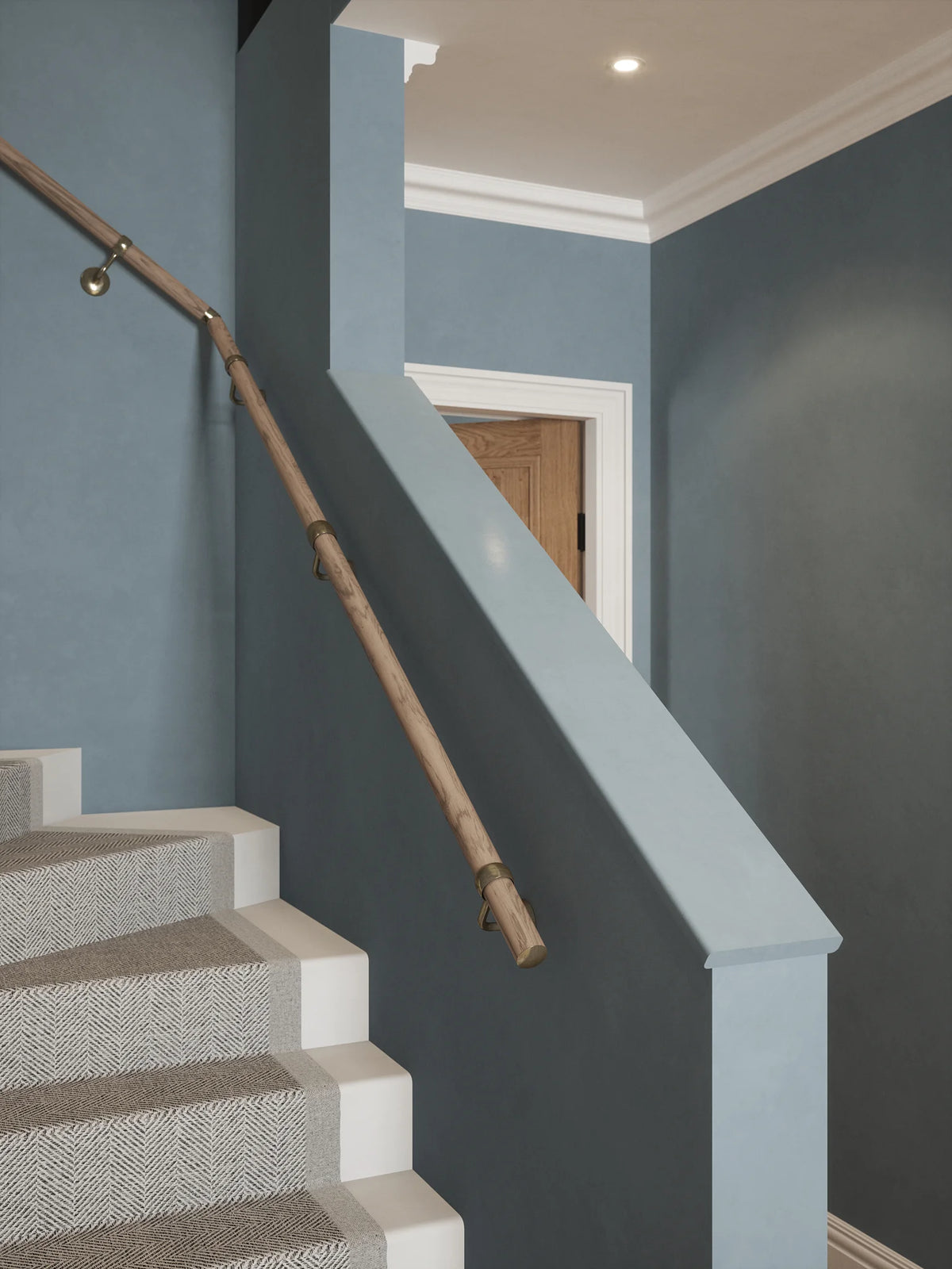 Front view of the Oversley Walnut Single Winder Handrail with Loxley Antique Brass brackets  beside a white-capped stair wall.