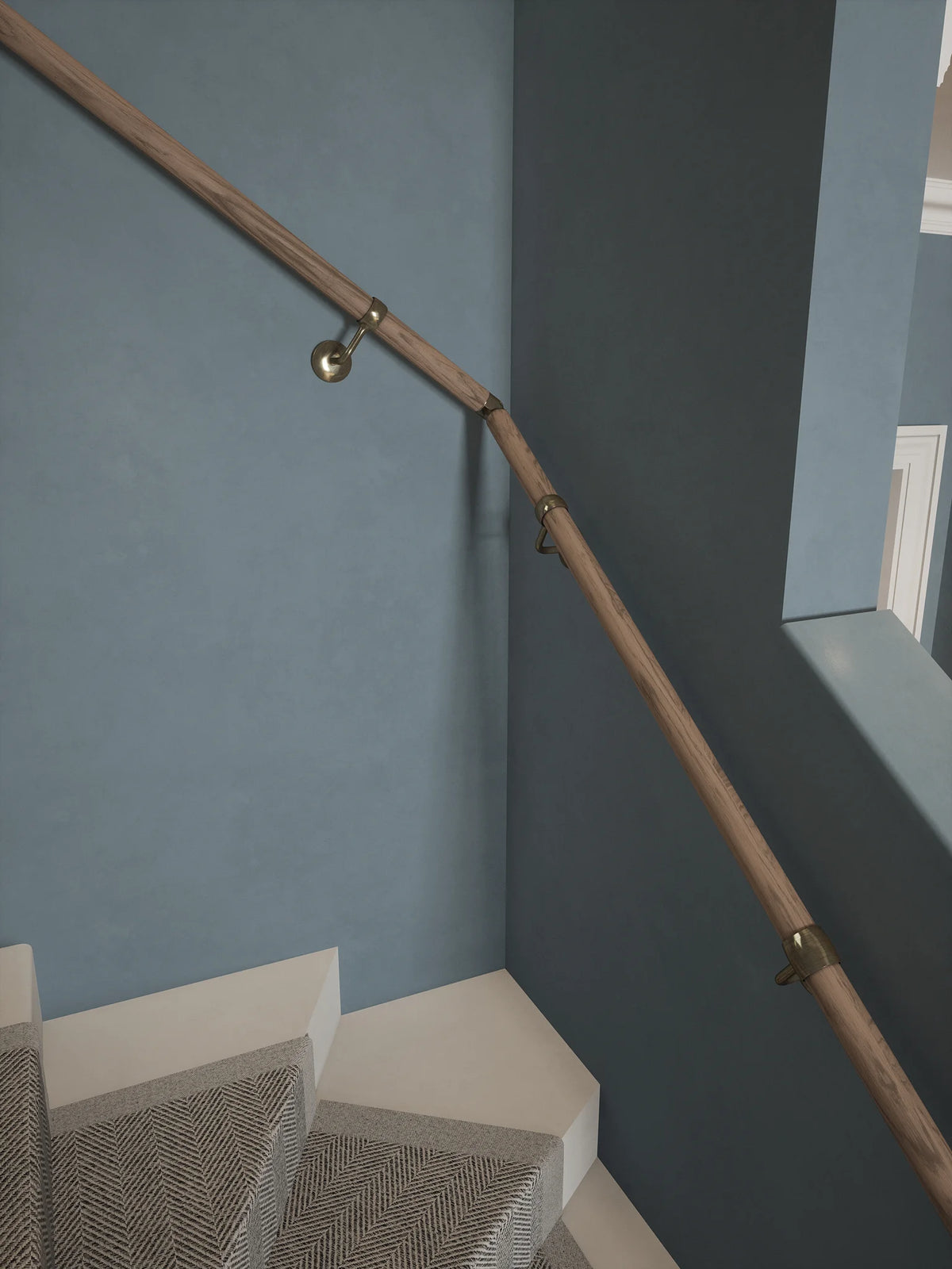 Close-up of the Oversley Walnut Single Winder Handrail with Loxley Antique Brass brackets on a blue-grey wall above carpeted turning steps.